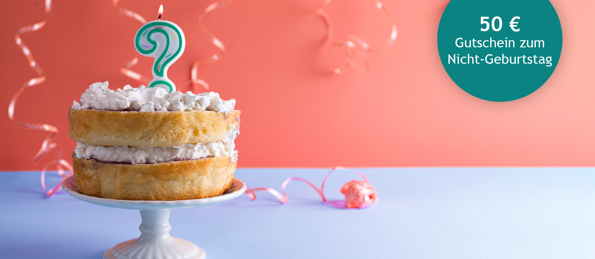 Eine mit Sahne und brennender Fragezeichen-Kuchenkerze verzierte Torte steht auf einem Kuchenteller. Im Hintergrund sind Luftschlagen und ein runder Störer mit dem Text: 50 € Gutschein zum Nicht-Geburtstag.